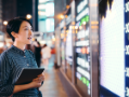 Asian businesswoman checking stock market data on tablet before Hong Kong financial display board.