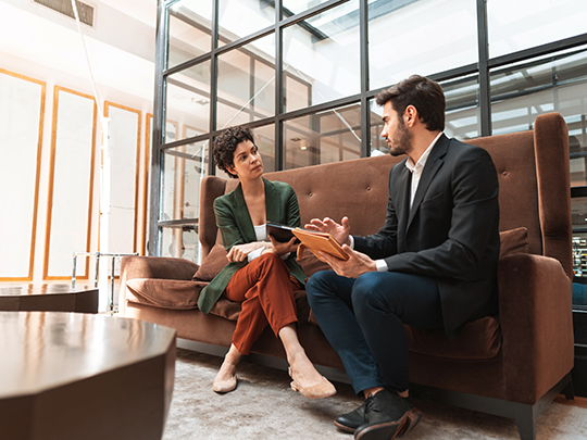 younger business colleagues sitting on tall brown sofa talking