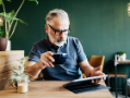 Man wearing glasses, holding cup and tablet.