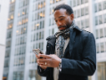 man with scarf holding phone in front of building