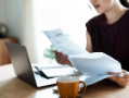 Woman examining papers with a cup of coffee and an open laptop.