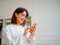 Woman in a white sweater holding a smartphone.