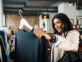 Woman in white jacket in a clothing store holding up a black blouse. 