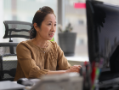 Woman sitting at a desk typing on a keyboard and looking at a large monitor.