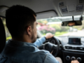 Backseat perspective of a young man driving a car