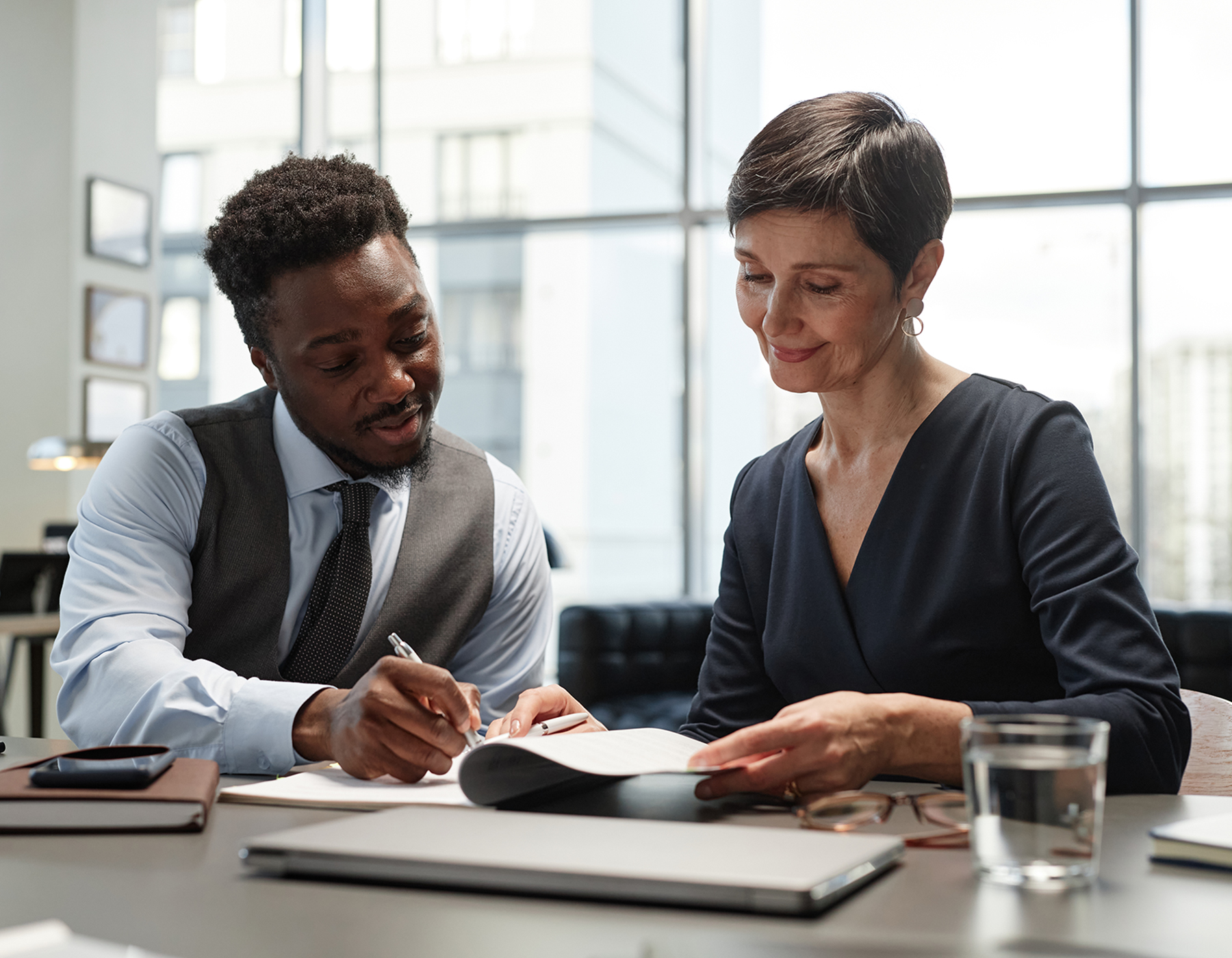 two diverse business colleagues reviewing documents at table in windowed office