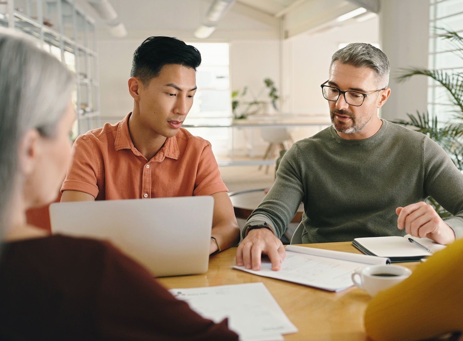 diverse multi-generational business team in meeting at desk with papers and laptop