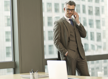 caucasian business man in suit talking on phone standing indoors in front of window