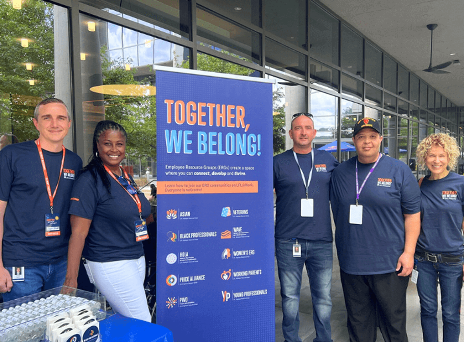 5 lpl coworkers standing outside lpl building with together, we belong sign