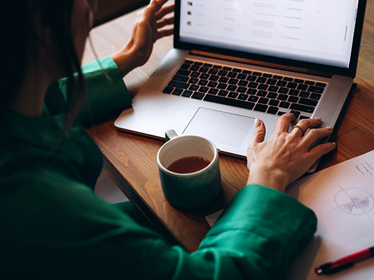 rear view of business woman in green shirt with arms extended out towards laptop