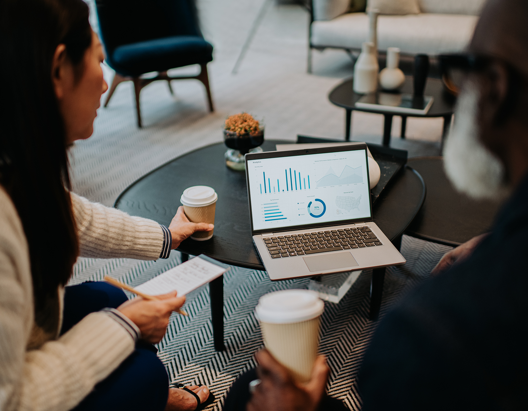 business colleagues, drinking coffee, meeting casually in common area with laptop showing graphs on lower table